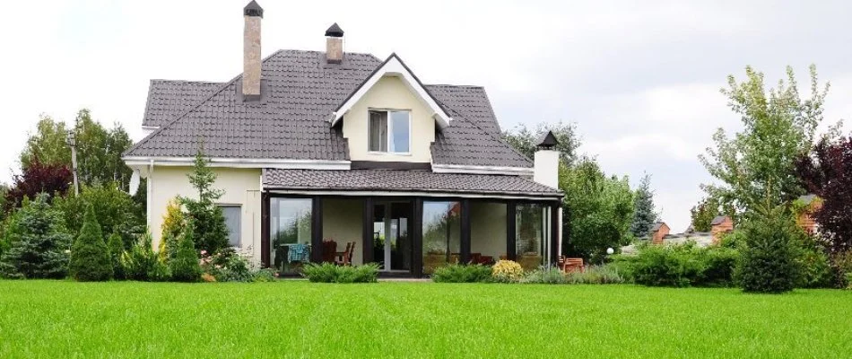  A well-maintained lawn in front of two houses, featuring a vibrant green grass area and a small tree with red foliage